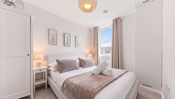 A bedroom with a bed, bedside tables, a window with curtains, and wall-mounted artwork. - Central Cosy Harrogate Apartment (North Yorkshire)