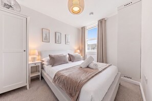 A bedroom with a bed, bedside tables, a window with curtains, and wall-mounted artwork.