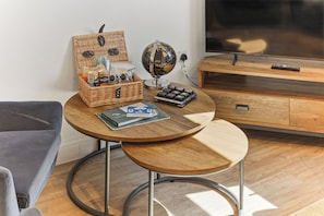 Une pièce avec une table ronde en bois, un globe terrestre, un panier rempli de collations, une télécommande et un téléviseur posé sur un meuble en bois.
