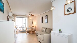 Ein modernes Wohnzimmer mit einer Couch, einem Esstisch und Stühlen. Es gibt einen Deckenventilator, eine kleine Kommode und eine Pflanze auf einem Beistelltisch.