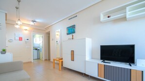 Ein modernes Wohnzimmer mit Flachbildfernseher, einer Couch, einem Holztisch und einer Küchenzeile im Hintergrund.