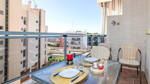Ein Balkon mit einem Glastisch, gedeckt für zwei Personen, zwei gestreiften Stühlen, einem roten Wasserkocher und einer kleinen Kuchenstück.