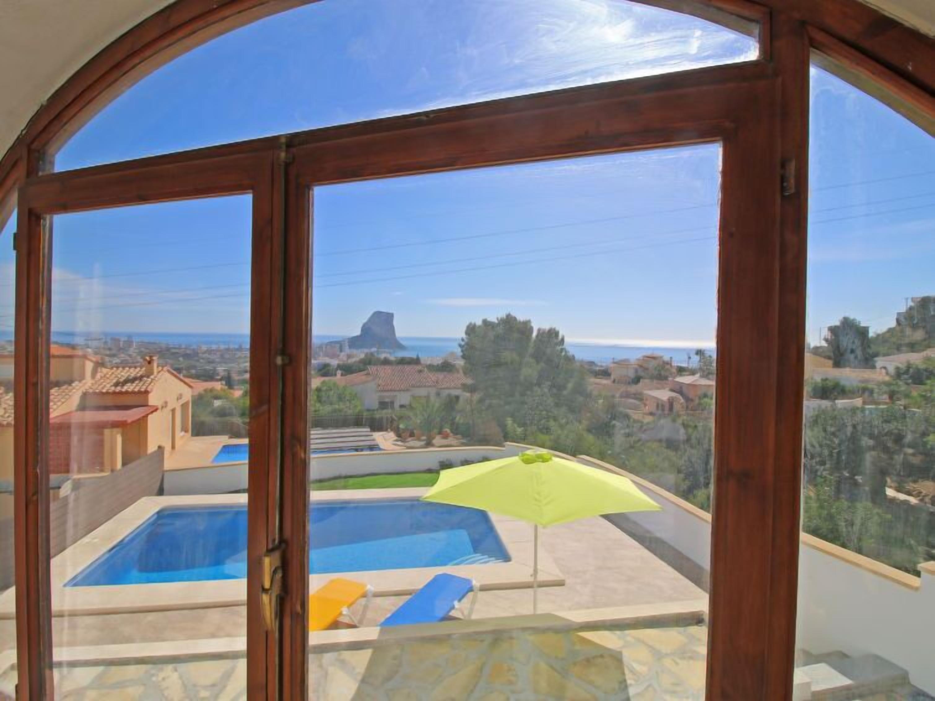 A view from a balcony with a swimming pool, a yellow umbrella, and a clear blue sky.