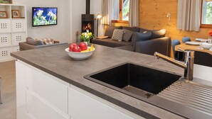 A modern kitchen with a built-in sink, a bowl of fruit, and a television in the background. - Sernisa Rez by Interhome (Verbier)