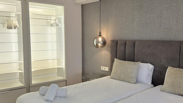 Habitación de hotel con dos camas, un armario grande con puertas de vidrio y una pared con textura.