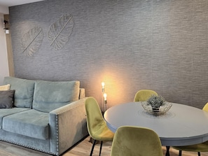 A modern living room with a grey sofa, green and yellow chairs, a round table with a plant, and a textured grey wall with leaf designs.