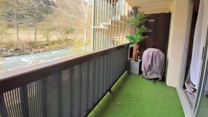 Un balcon avec vue sur une rivière et des montagnes, une plante en pot et un espace barbecue abrité.