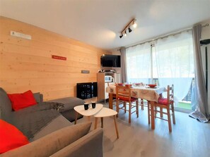 Una sala de estar acogedora con un sofá, una mesa de comedor preparada para cuatro comensales y una zona de cocina con microondas y televisor de pantalla plana.