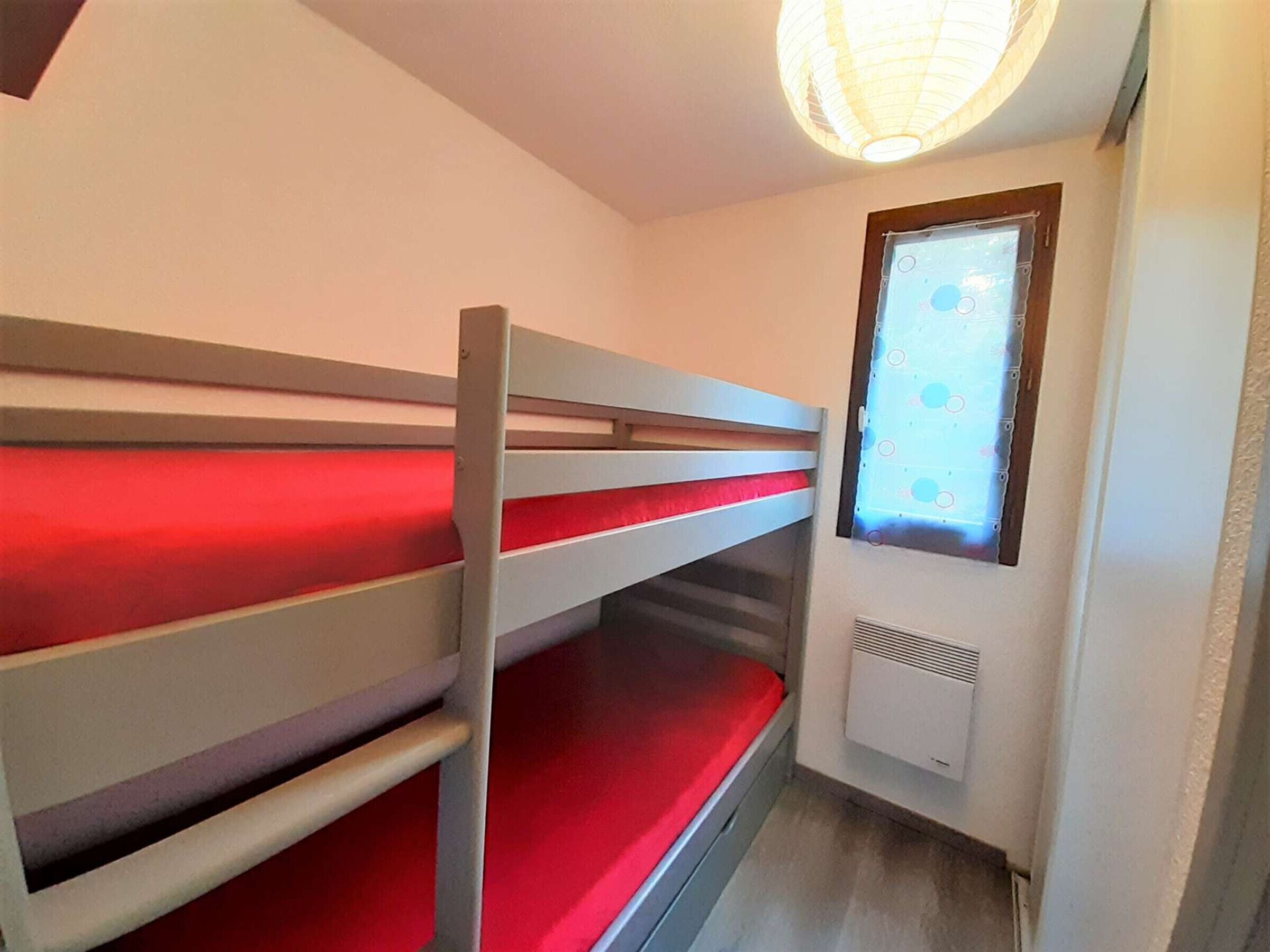 Une chambre avec un lit superposé, une fenêtre et un radiateur.