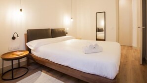 Moderni hotellihuone, jossa on suuri sänky, yöpöytä, peili ja ovi.