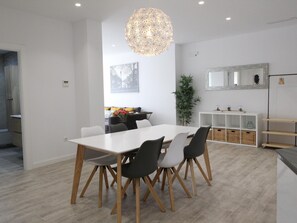 A modern dining area with a white table and chairs, a hanging light fixture, a plant, and a mirrored cabinet.