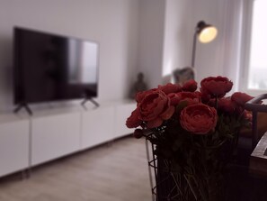 A living room with a flat-screen TV on a stand, a vase with red flowers, and a floor lamp. - 3-bed, 2-bath apartment, equipped kitchen, central Malaga (Málaga)