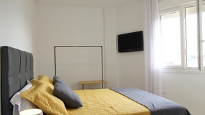 A bedroom with a bed, a bedside table, a lamp, a TV on the wall, and a window with curtains.