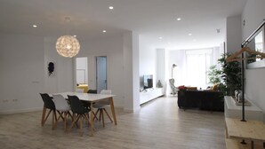 A spacious living area with a dining table, chairs, a sofa, and a staircase.