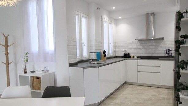 A modern kitchen with white cabinets, a stainless steel range hood, and a black countertop.