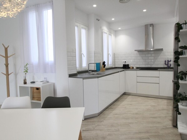 A modern kitchen with white cabinets, a stainless steel range hood, and a black countertop.