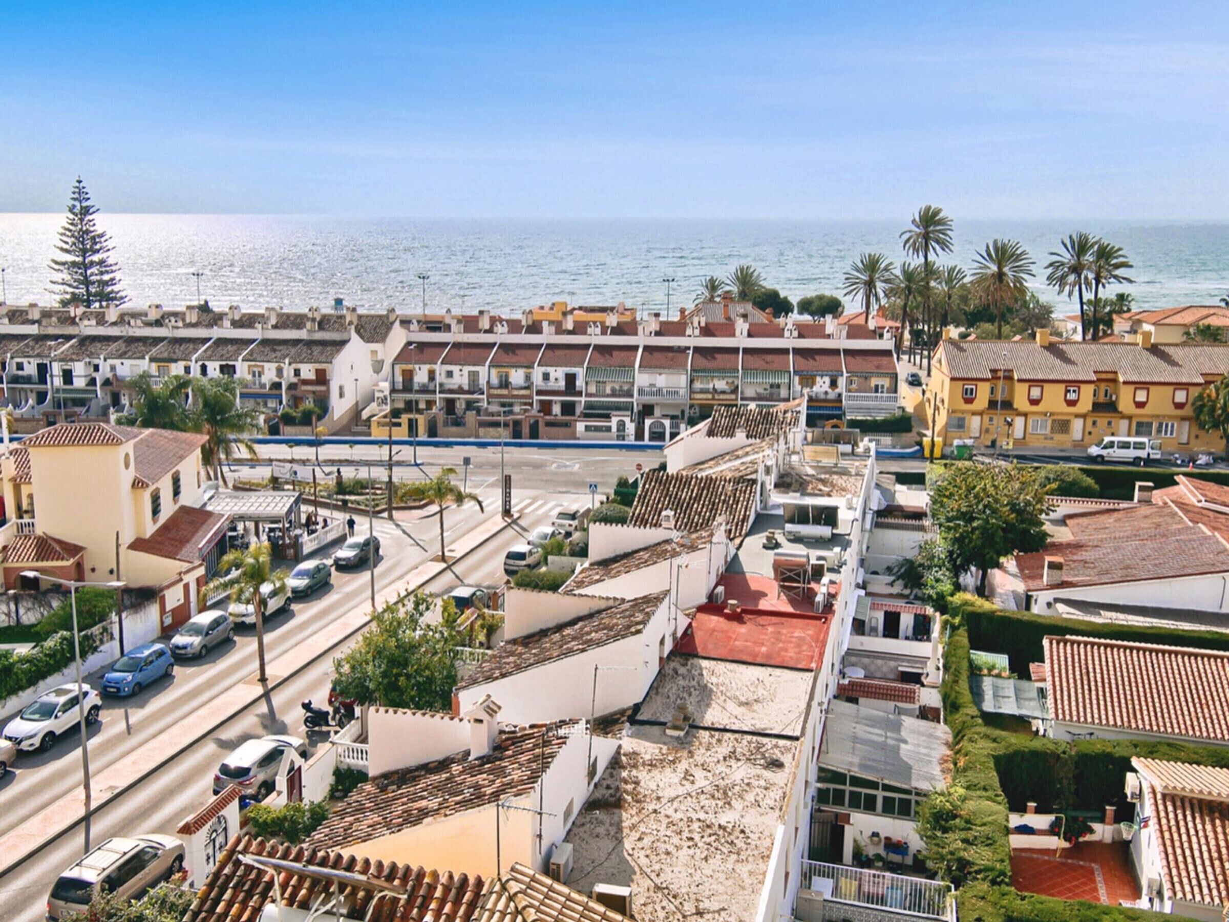 Una zona costiera urbana caratterizzata da case a schiera, una strada con veicoli e una vista limpida sul mare.