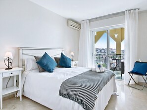 A hotel room with a bed, two bedside tables, a balcony with a chair, and a city view. - Beachfront apartment with pool in Rincón de la Victoria (Rincón de la Victoria)
