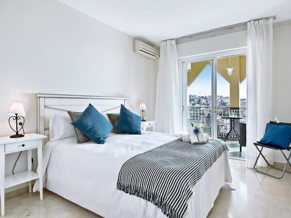 A hotel room with a bed, two bedside tables, a balcony with a chair, and a city view. - Beachfront apartment with pool in Rincón de la Victoria (Rincón de la Victoria)
