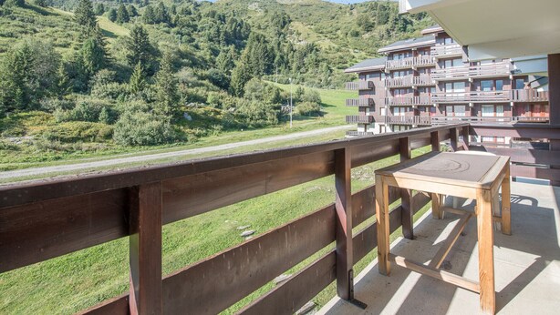Un balcón con vistas a un paisaje montañoso y un edificio de varios pisos con balcones.