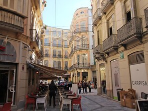 A narrow street with outdoor seating, a restaurant, and a building with a 'CARPISA' sign.