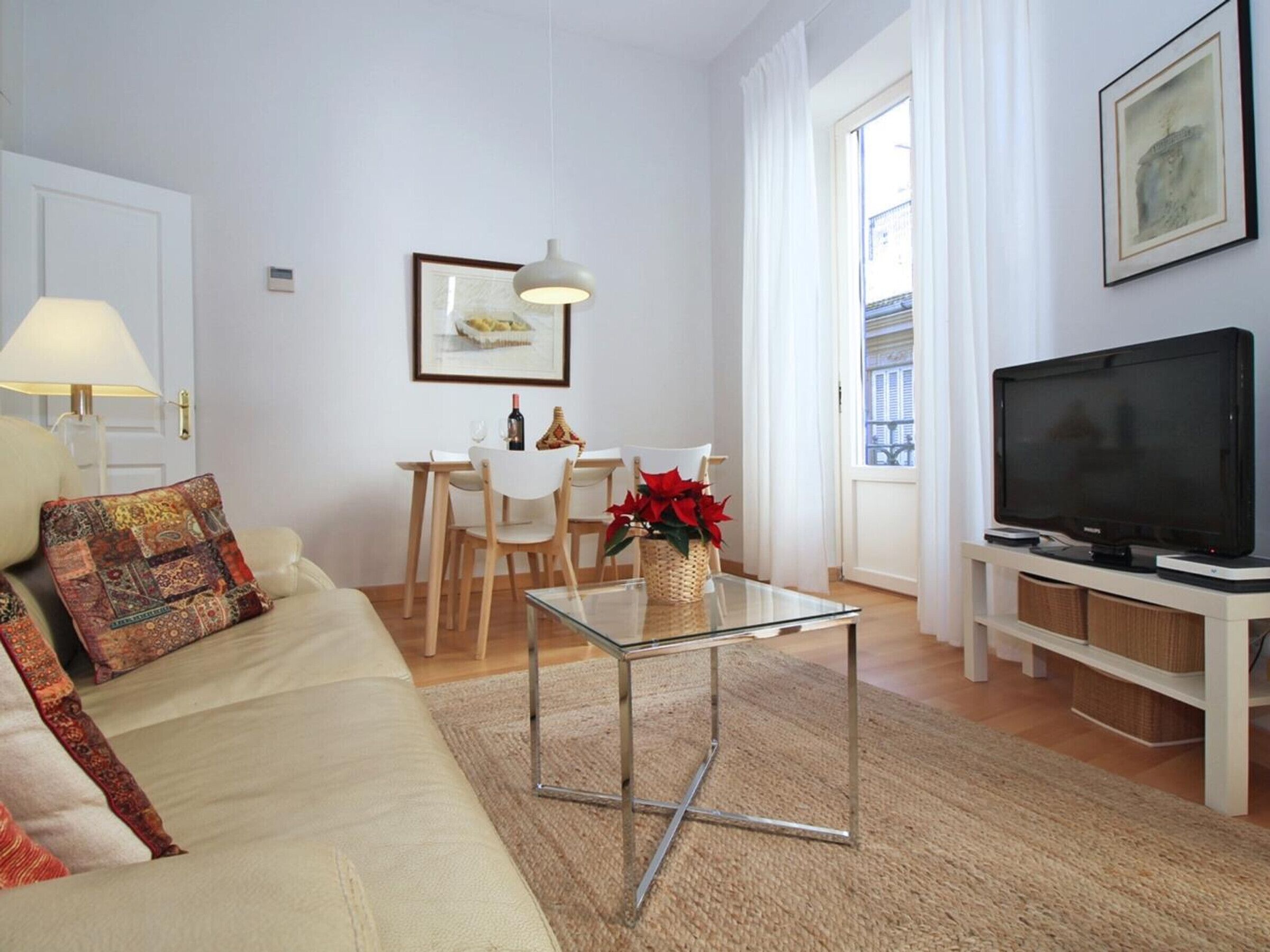 Een woonkamer met een bank, een glazen salontafel, een eettafel met stoelen, een televisie en een raam met gordijnen.