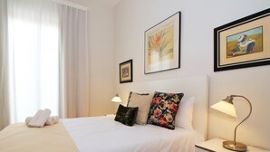 Una camera d'albergo con un letto, due lampade sui comodini, un comodino, una finestra con tende e due quadri appesi al muro.