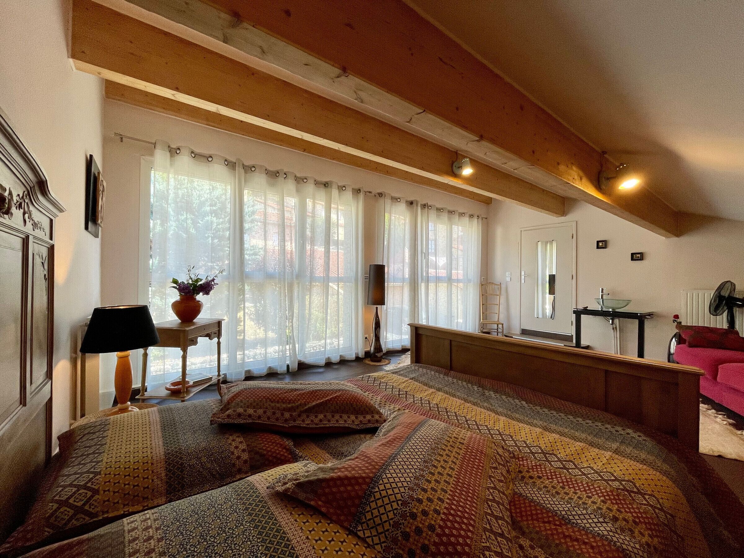 Une chambre à coucher avec un grand lit, une table de chevet avec une lampe, une chaise et une fenêtre avec des rideaux.