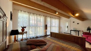 Un dormitorio con una cama grande, una mesita de noche con una lámpara, una silla y una ventana con cortinas.