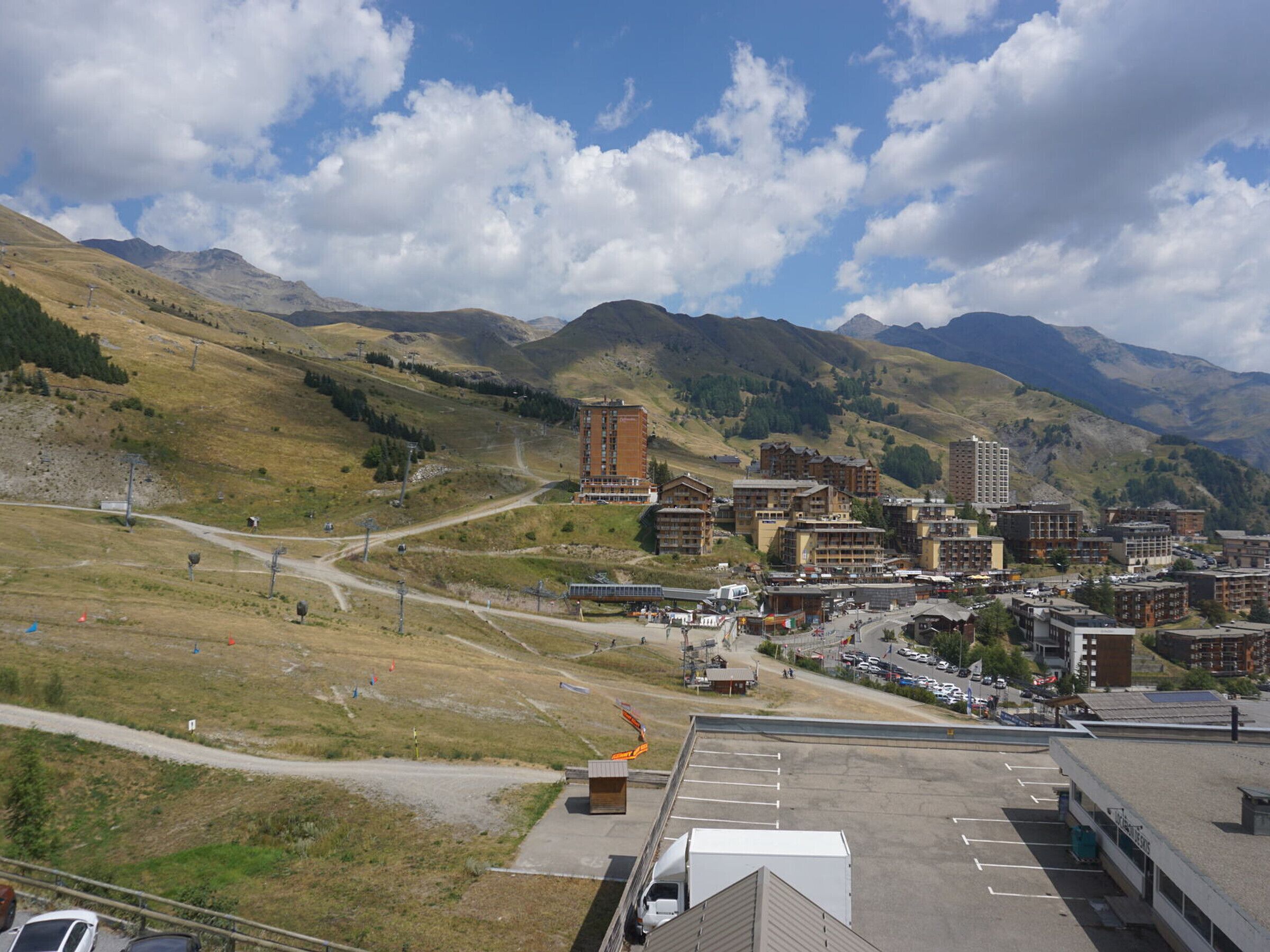 A mountainous town with a mix of modern and traditional buildings, a parking lot, and a clear sky.