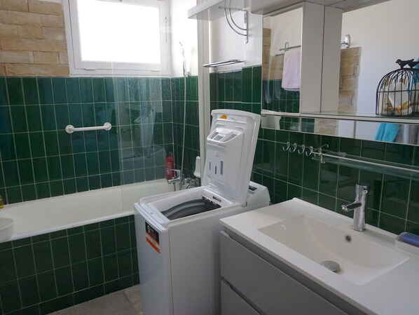 Un baño con lavadora blanca, un lavabo y una mampara de cristal para la ducha.