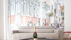 Een woonkamer met een bank, een glazen salontafel met een fles champagne en een kleurrijke muurschildering op de achtergrond.