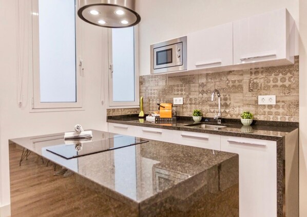 A modern kitchen with a central island, white cabinets, a microwave, and a patterned backsplash. - Charming 1BR Apartment in the Heart of Málaga - Near Mercado de Atarazanas (Málaga)