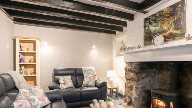 A cozy living room with a fireplace, a black leather sofa, a wooden coffee table, and a bookshelf. - Llys Mair (Bala)