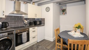 A modern kitchen with white cabinets, a black countertop, a built-in oven, a washing machine, and a dining area with a table set for two. - Llys Mair (Bala)