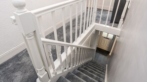 A staircase with white balusters and a handrail, carpeted steps, and a door at the bottom. - Llys Mair (Bala)