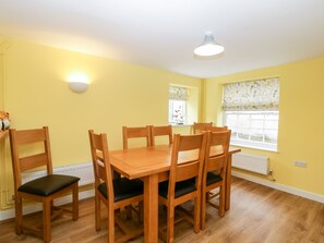 A dining area with a wooden table and chairs, a ceiling light, and a window with curtains. - Granary Cottage (Warminster)