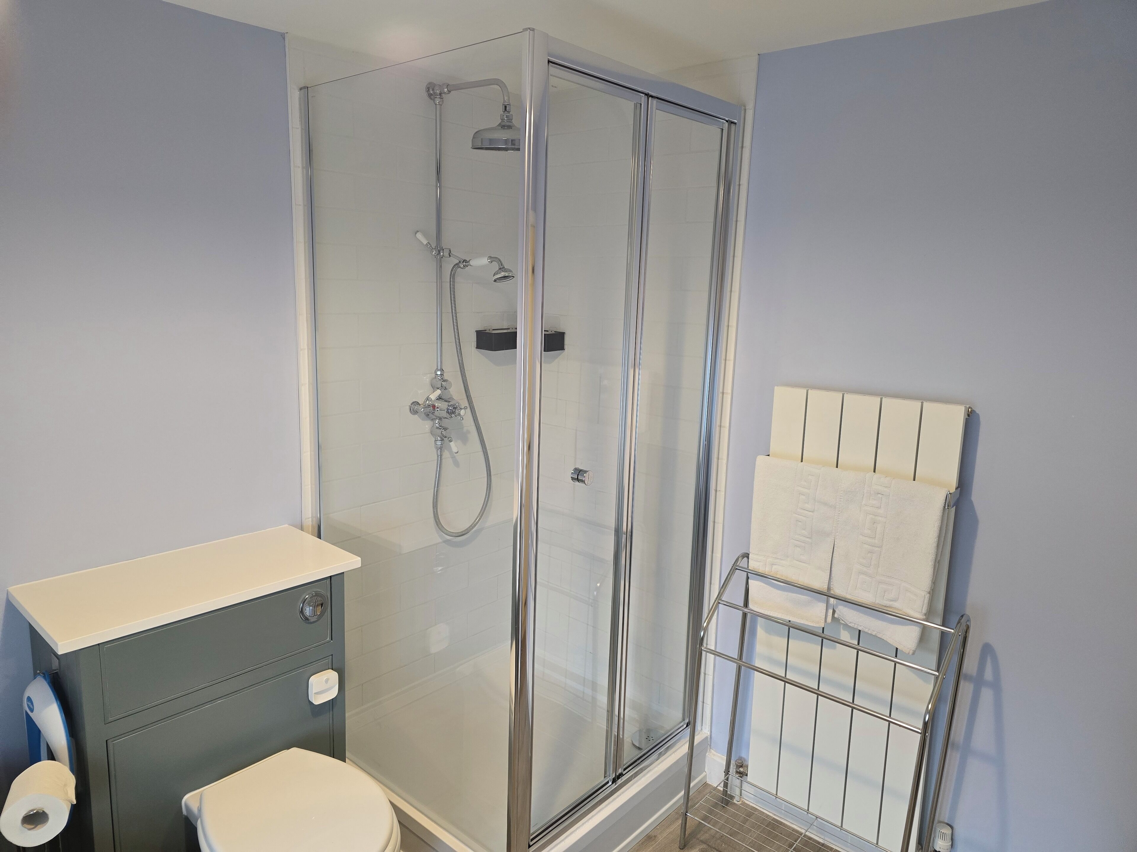 Un baño con ducha de vidrio, inodoro y perchero para toallas.