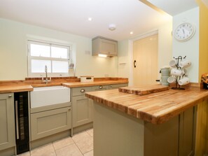 A modern kitchen with wooden countertops, a built-in dishwasher, and a wall-mounted clock. - Granary Cottage (Warminster)