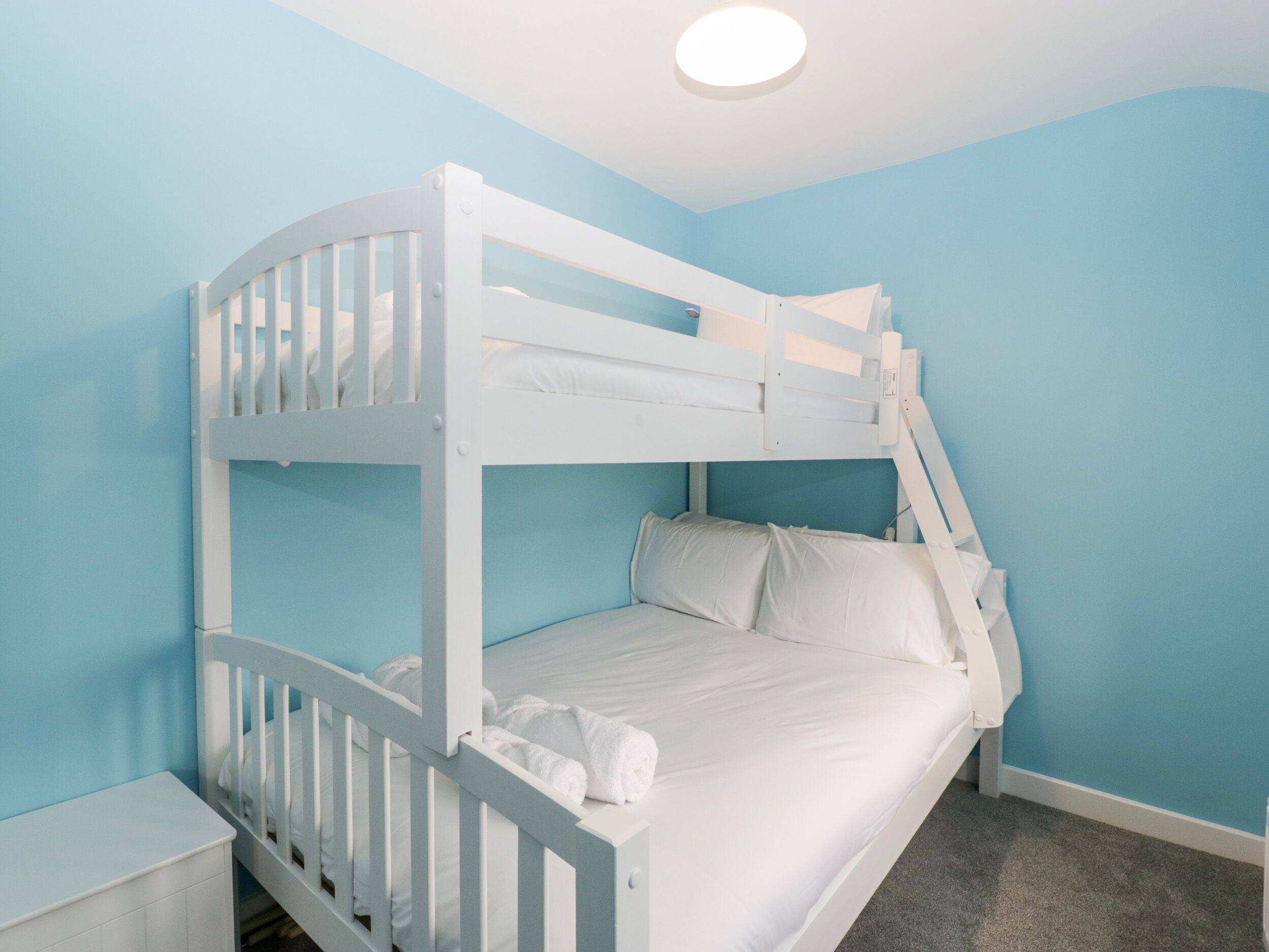 Un lit superposé dans une chambre aux murs bleu clair et dotée d’un luminaire blanc au plafond.
