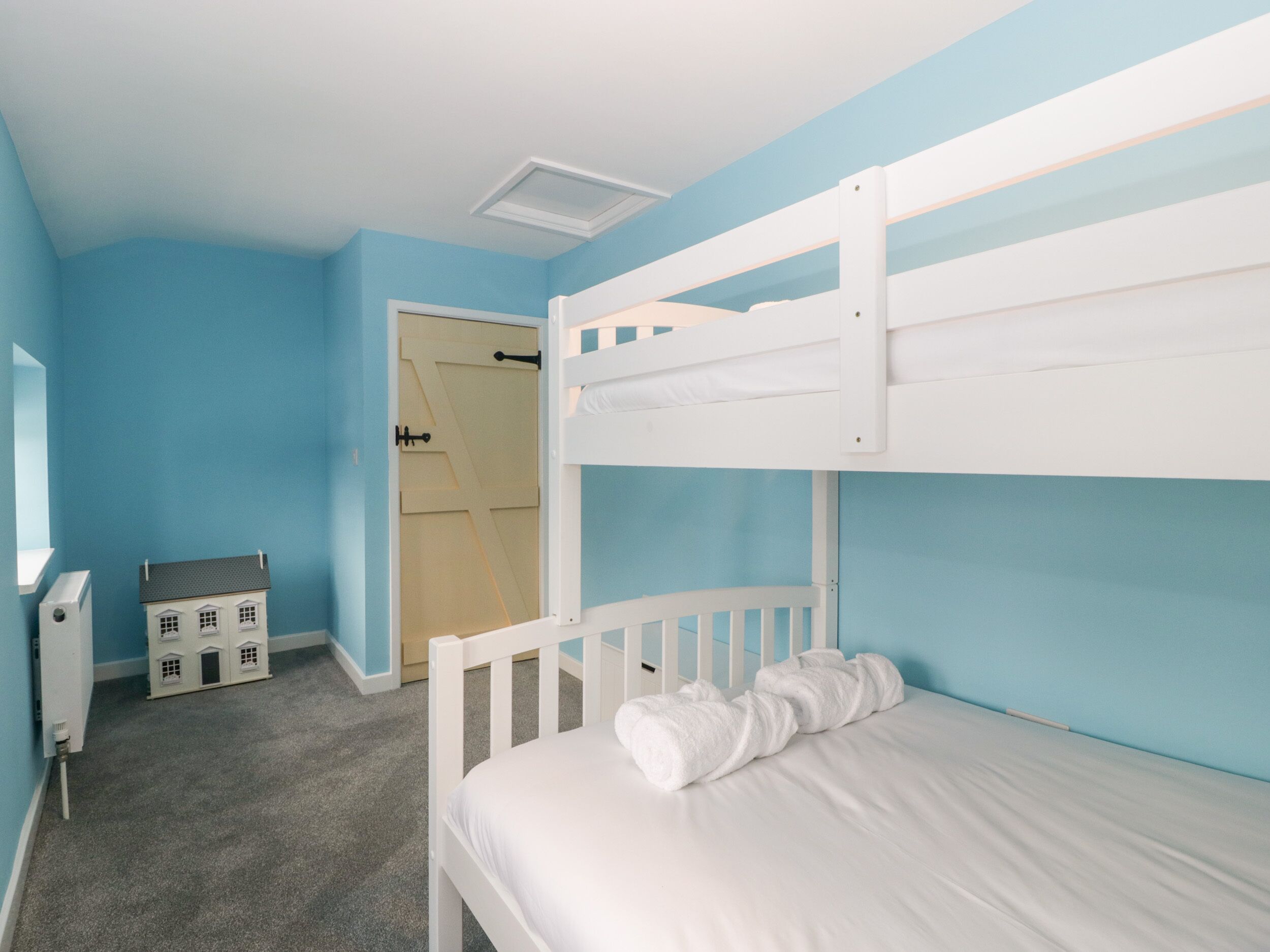 Ein Schlafzimmer mit Etagenbetten, einer Tür zu einem weiteren Raum, einem kleinen Spielhäuschen und einem Heizkörper.