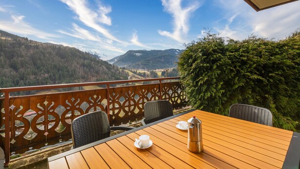Una mesa de madera con sillas y vistas a un paisaje montañoso.