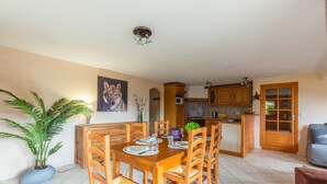 Un comedor con una mesa y sillas de madera, una planta en maceta y una cocina al fondo.