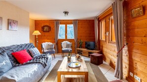 Una habitación acogedora con un sofá, una mesa con un plato de comida, una silla, un televisor y paredes de madera.