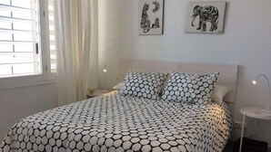 Ein Schlafzimmer mit einem Bett, zwei Wandbildern, einem Nachttisch mit Lampe und einem Fenster mit Vorhängen.