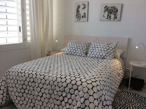 A bedroom with a bed, two wall art pieces, a bedside table with a lamp, and a window with curtains.