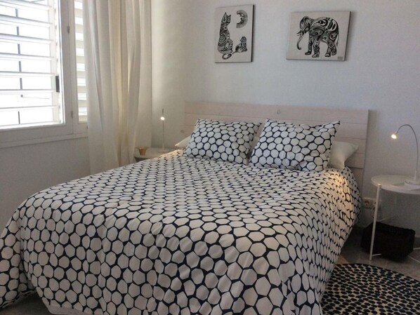A bedroom with a bed, two wall art pieces, a bedside table with a lamp, and a window with curtains. - Guadalmar: Beach, Pool, Golf, Relax (Málaga)