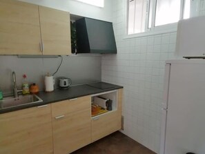 A kitchen with wooden cabinets, a black microwave, a sink with a faucet, and a white refrigerator. - Guadalmar: Beach, Pool, Golf, Relax (Málaga)