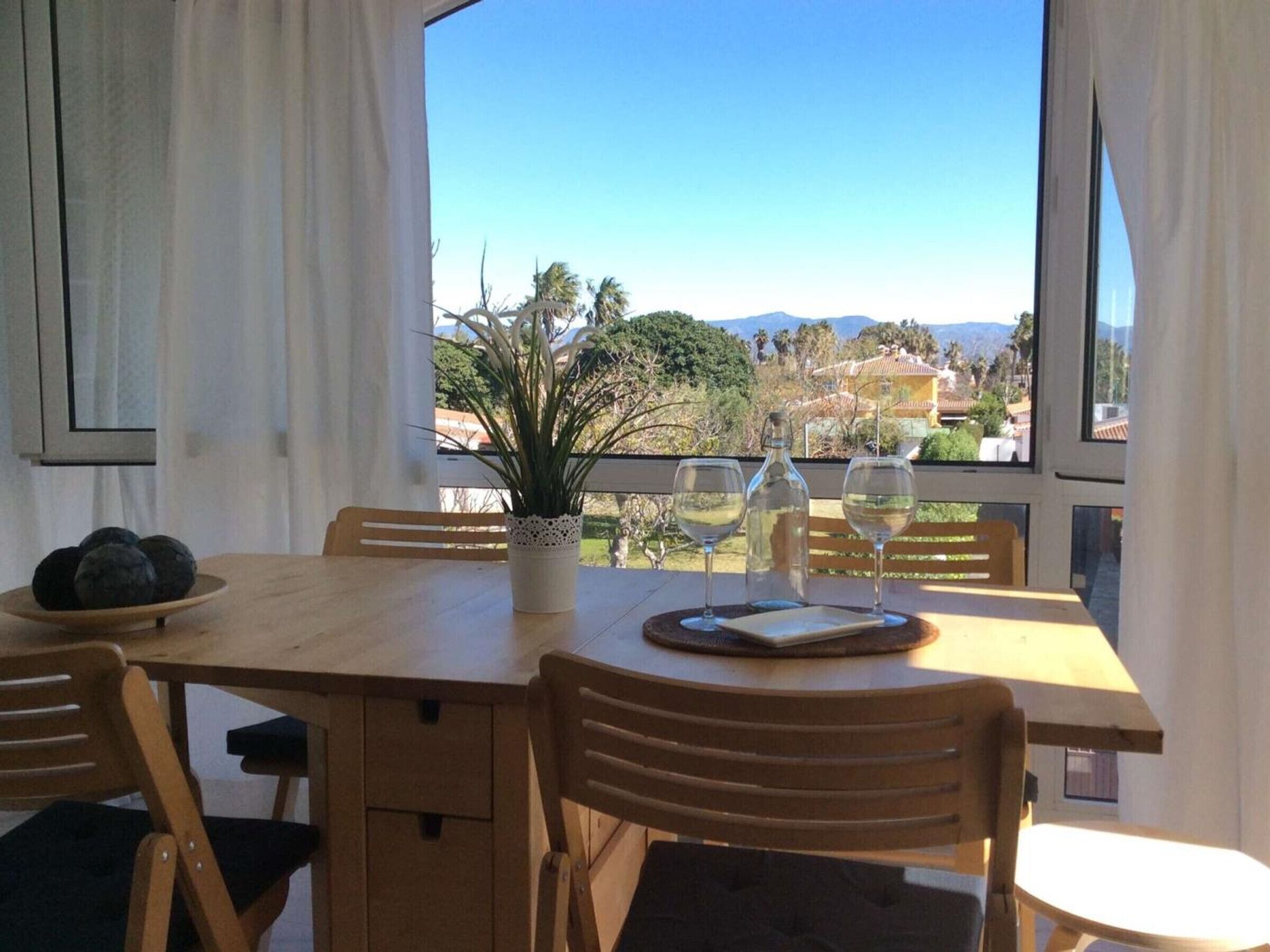 Ein Essbereich mit einem Tisch für zwei Personen, einem Blumentopf und einem schönen Ausblick auf Hügel und Bäume.