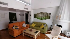 Ein geräumiges Wohnzimmer mit großem Fenster, einem grünen Sofa, einem orangen Sofa, einem weißen Sessel und einem Couchtisch.